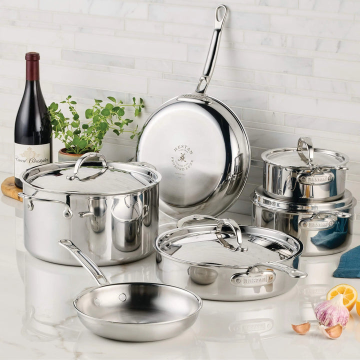 Set of stainless steel cookware on a kitchen counter with a bottle of wine and plants in the background.