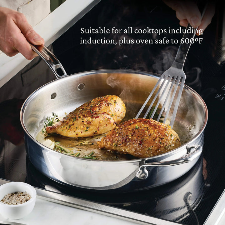 Stainless steel frying pan with cooked chicken on a stovetop, with text about cooktop compatibility.