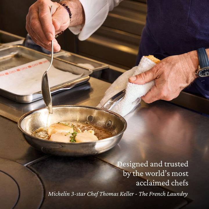 Person cooking in a professional kitchen with a pan on a stove, using a spoon.